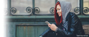 Picture of a red-headed girl smiling while looking at her phone, wearing a hoodie
